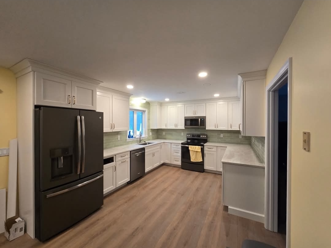 Finished kitchen with white cabinets, black appliances and green backsplash after renovation